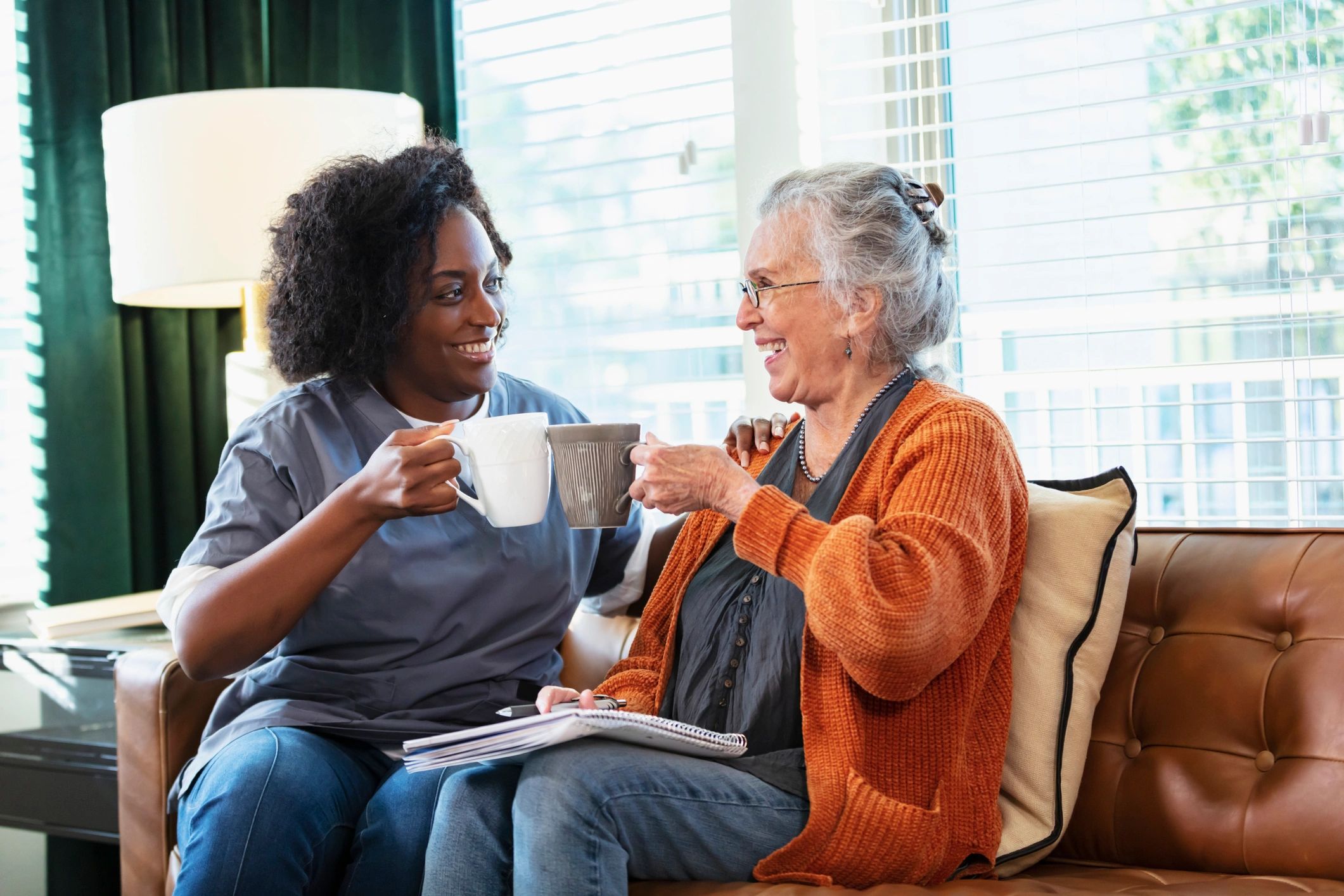 Caregiver and senior woman talking together at home in a living room