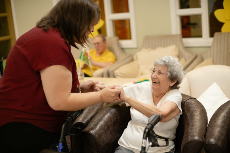 A caregiver holding hands with a smiling elderly woman in a care setting